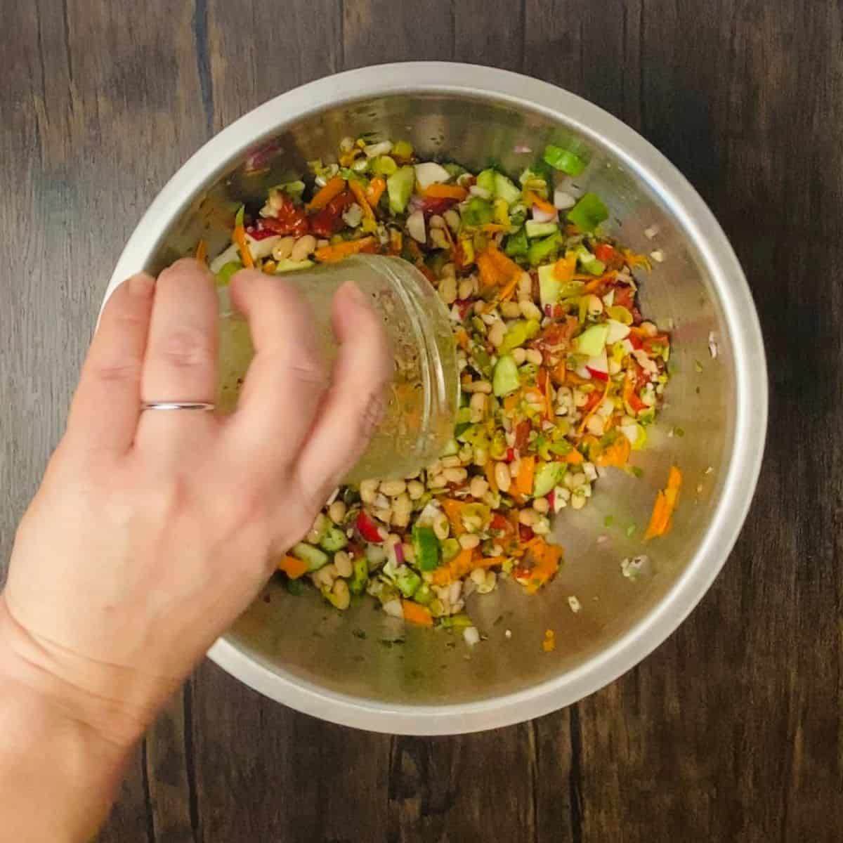 A hand pouring the dressing ingredients into the bowl of salad ingredients.