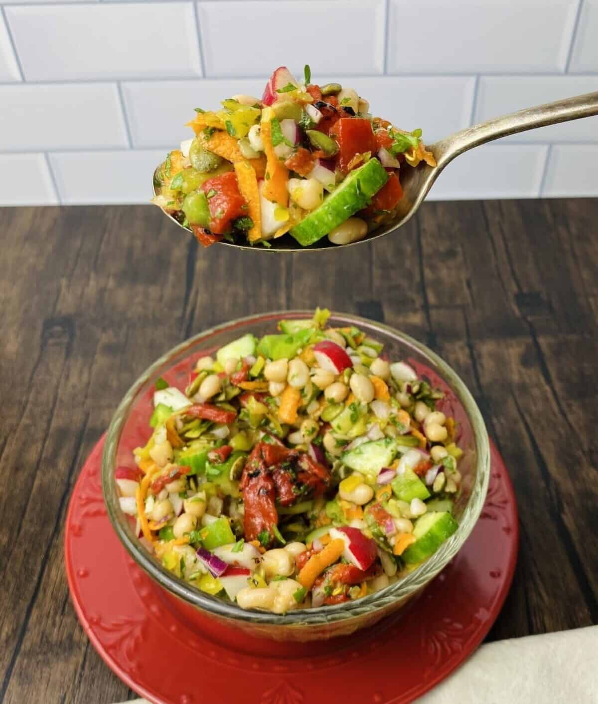 A spoon filled with chopped salad hovering above a bowl of salad.