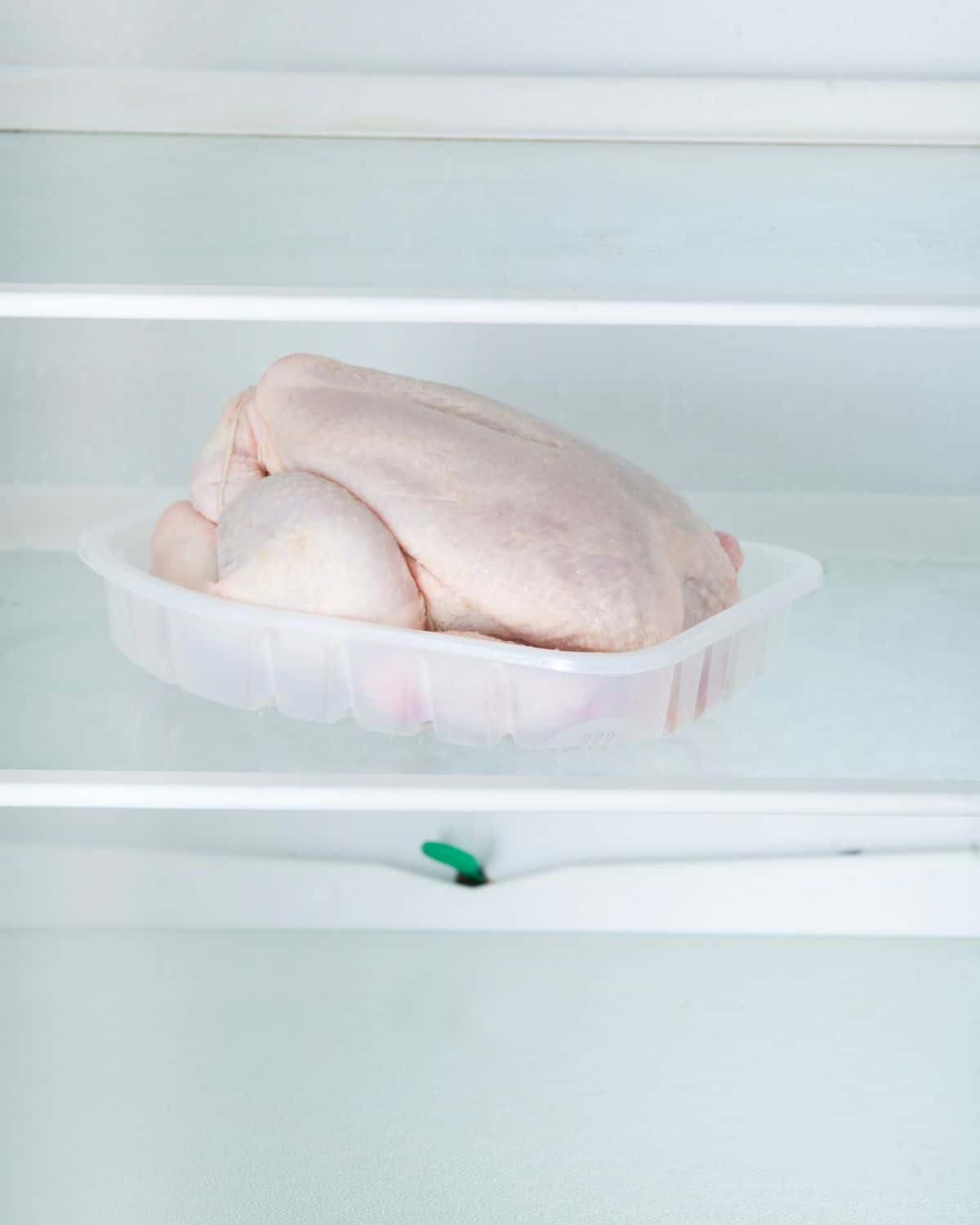 A whole raw chicken thawing in the refrigerator.