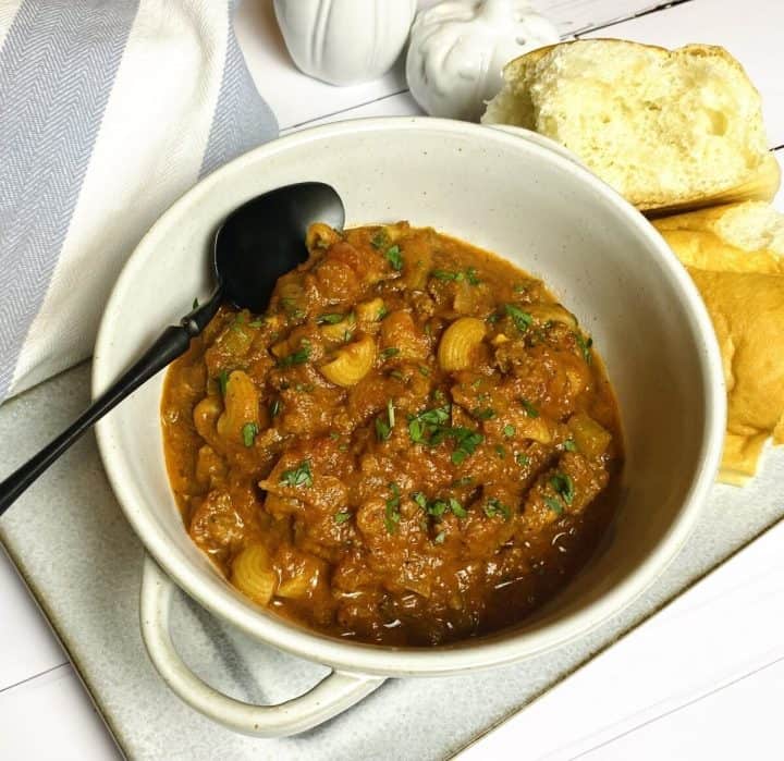 Bowl of one pot american goulash with a spoon and a side of bread.