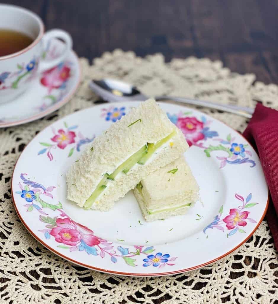 Two traditional cucumber sandwiches on a pretty plate with a cup of tea.