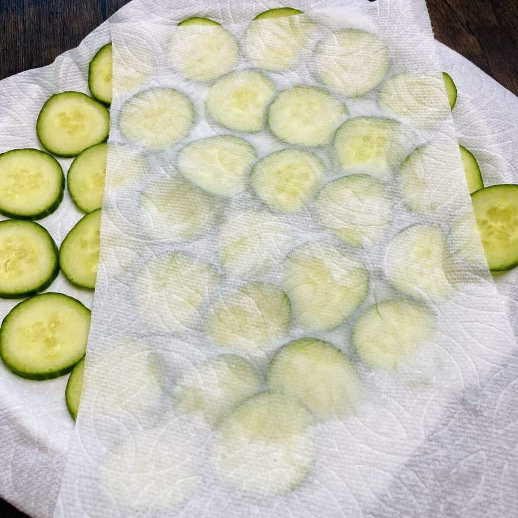 Cucumber slices being dabbed with a paper towel.