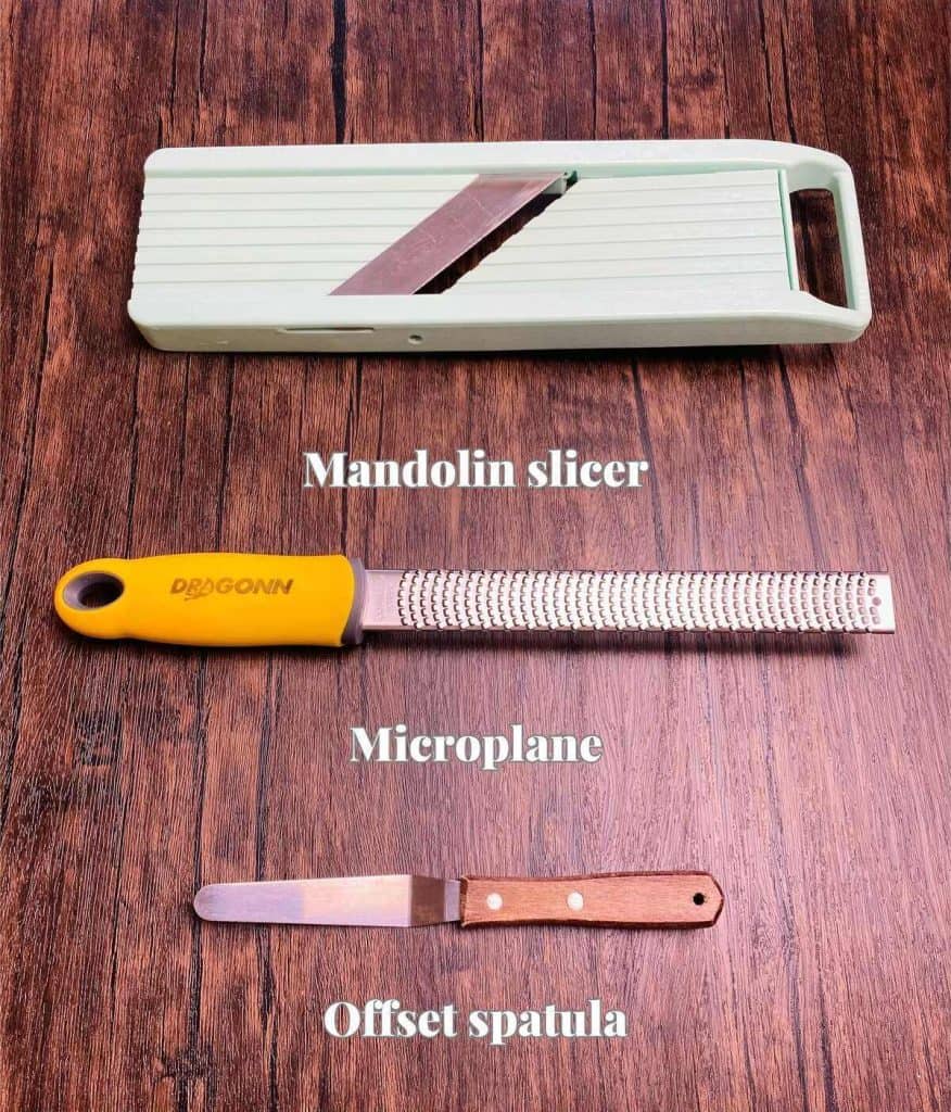 A mandolin slicer, microplane, and offset spatula on a wood table.