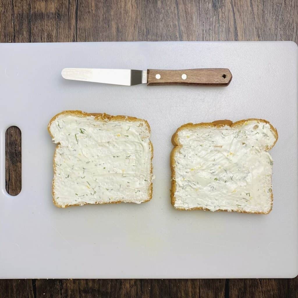 Two slices of bread spread with cream cheese mixture alongside an offset spatula.