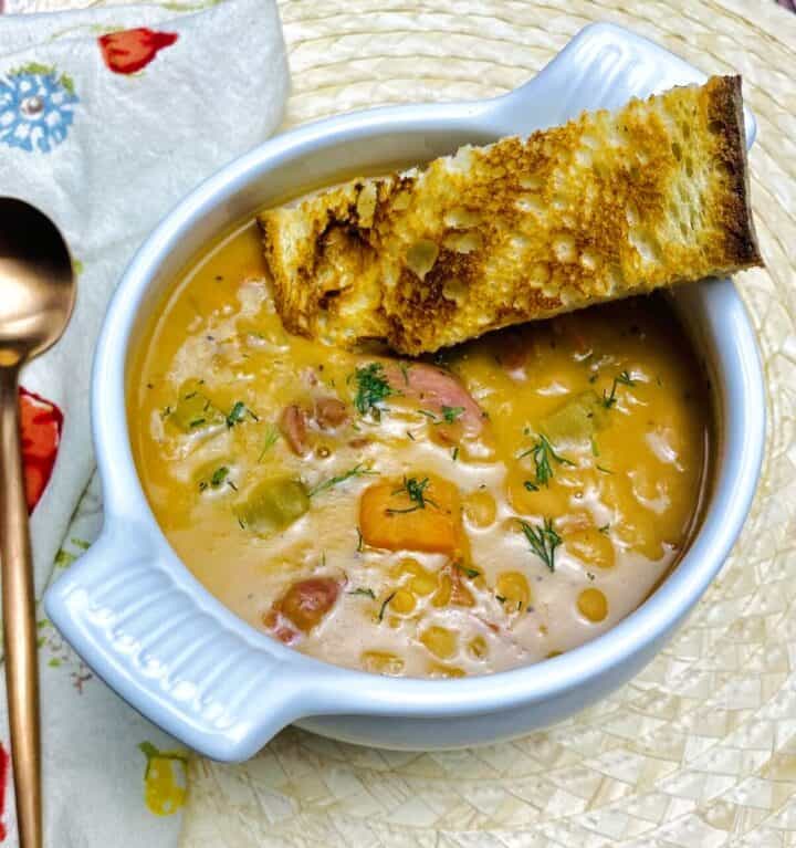 Bowl of ham and beans with grilled bread dunked in it.