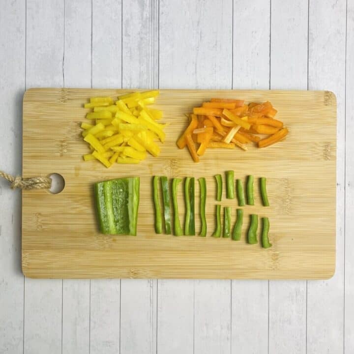 Bell peppers on a cutting board sliced into strips.