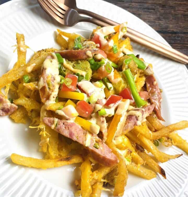 A pile of dirty fries on a dinner plate with silverware.