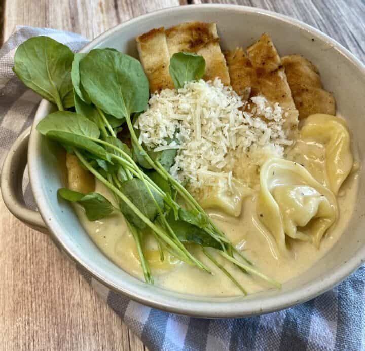 A closeup of a prepared bowl of Chicken tortellini alfredo soup.