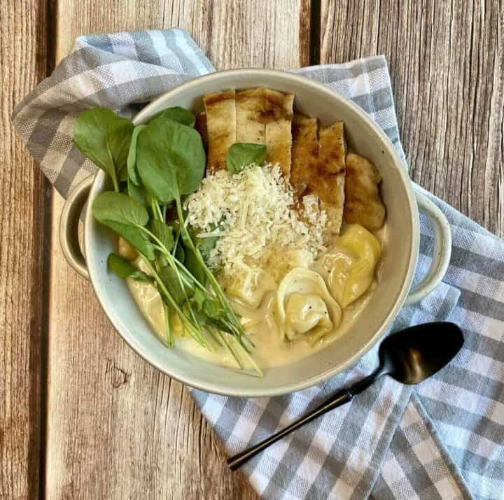 A bowl of chicken alfredo soup with a napkin and a spoon.