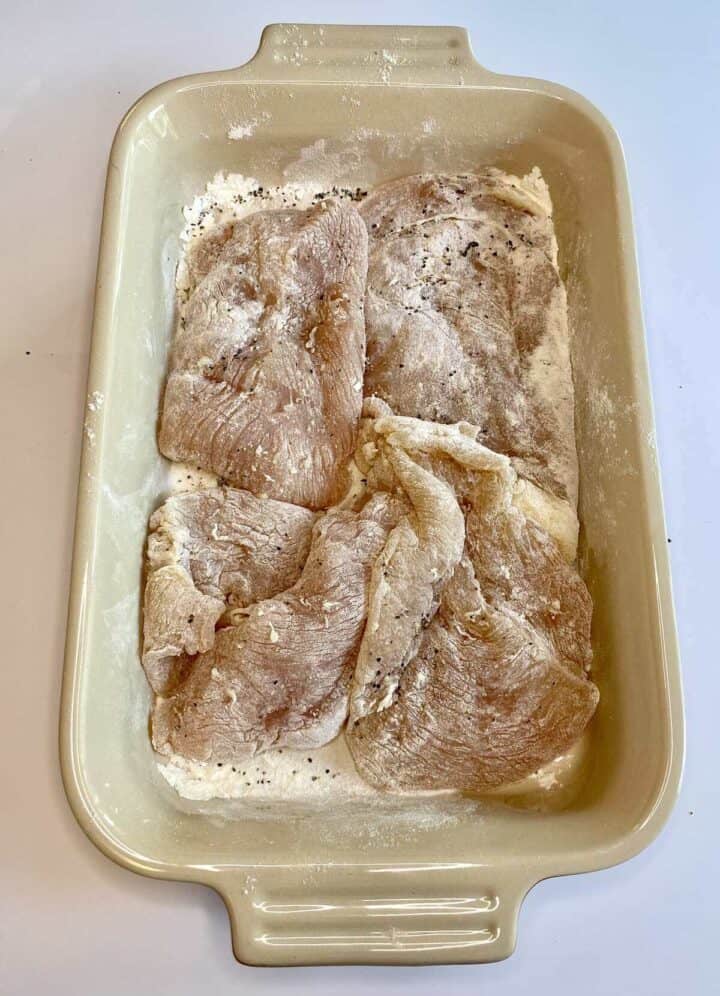 A tray filled with raw chicken dusted in flour and seasonings.