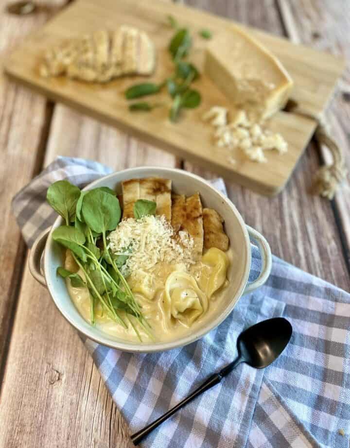 A bowl of soup with a tray of parmesan cheese nearby.