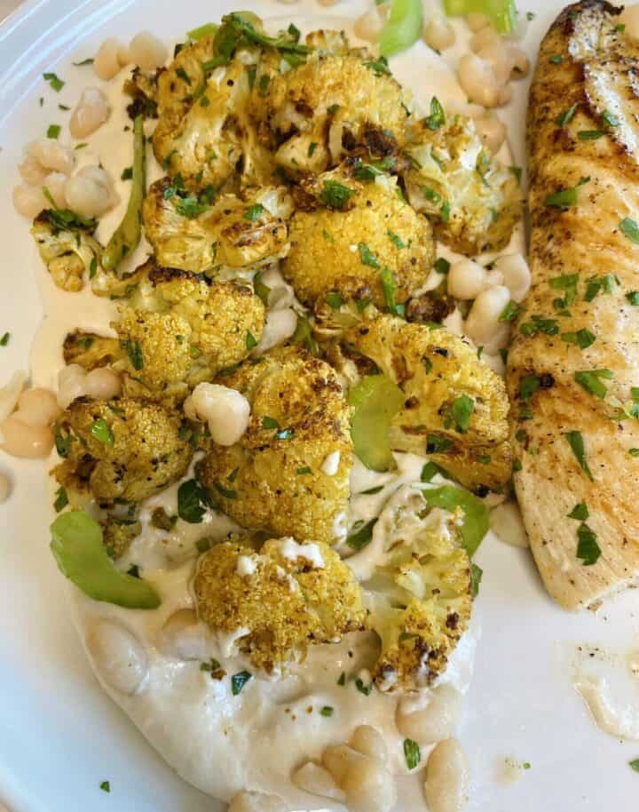 Roasted spiced cauliflower on white bean hummus on a plate with chicken.