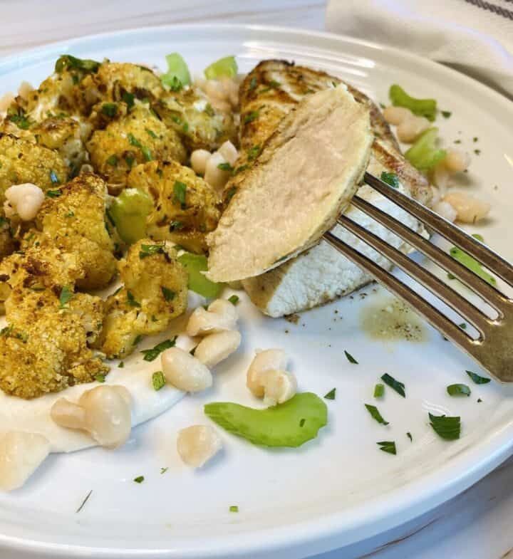 A fork holding up a peice of cooked chicken over a plate.