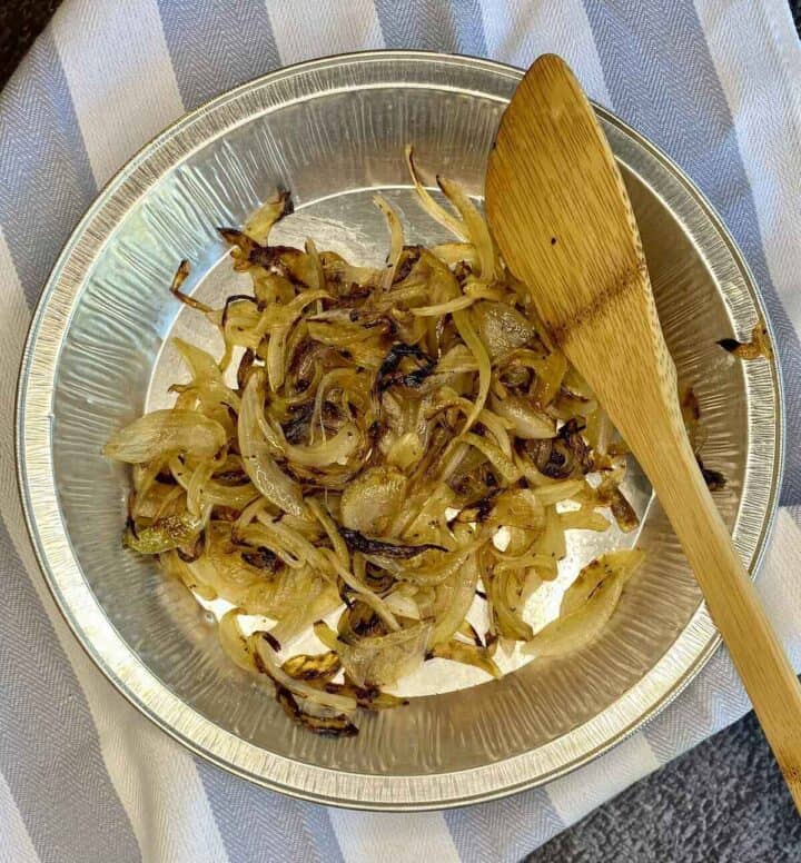 An aluminum pan filled with griddled onions and a wooden spoon.