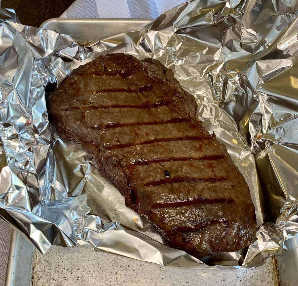 Grilled flat iron steak resting on a pan lined with tin foil.