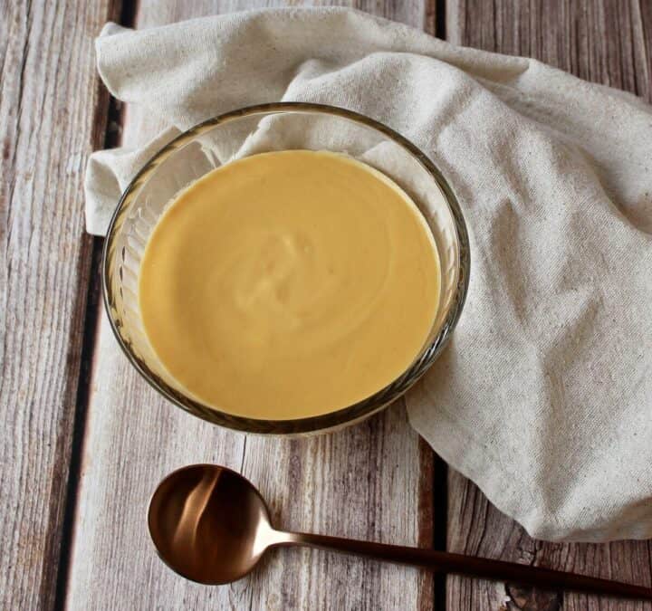 Cheese sauce in a clear bowl with a spoon and napkin.