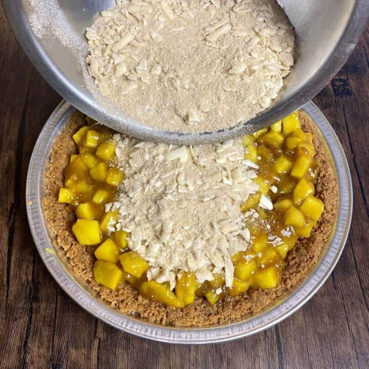 A bowl of crumb topping being poured on top of the pie.