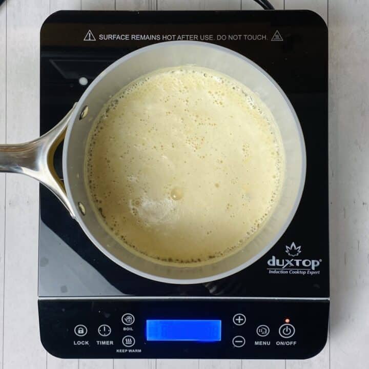 A pot of cheese sauce starting to simmer on a burner.