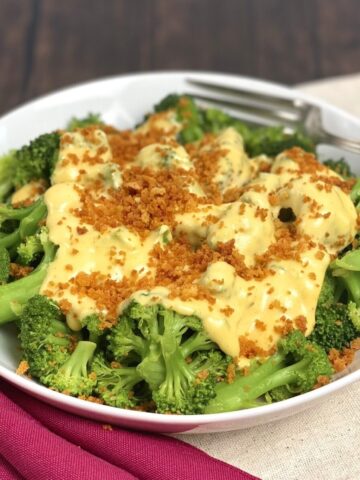 A bowl of cooked broccoli covered in cheese sauce and panko.