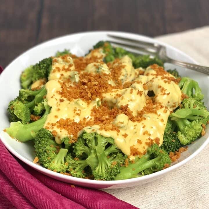 A bowl of cooked broccoli covered in cheese sauce and panko.