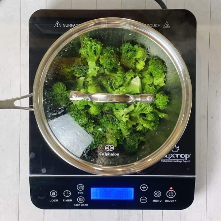 A pot on a burner with a lid and steamed broccoli.