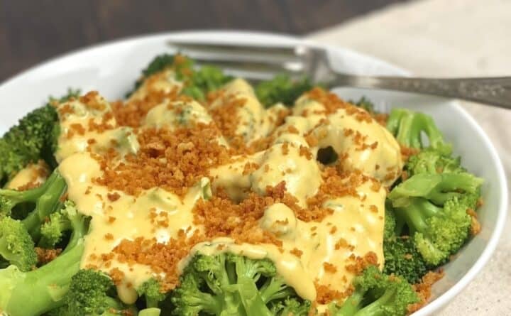 A close up view of cheesy broccoli in a dish with panko topping and a fork.