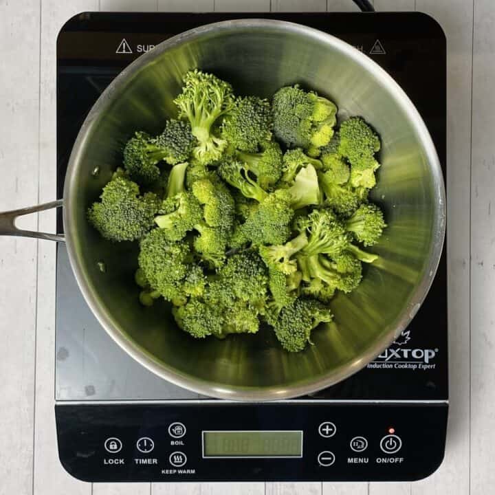 A pot on a burner with raw broccoli and a little water.