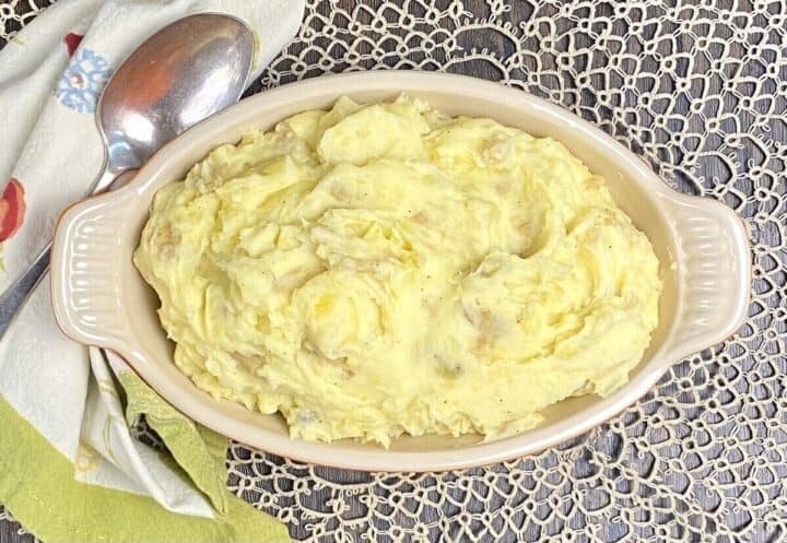 An oval dish of rustic mashed potatoes with a spoon and napkin.