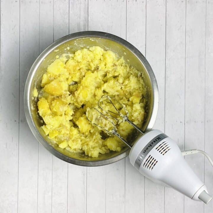 A bowl of potatoes being mashed by hand beaters.