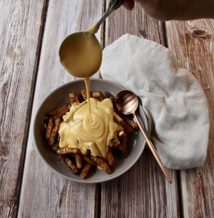 Cheese sauce no flour being poured over a pile of french fries.