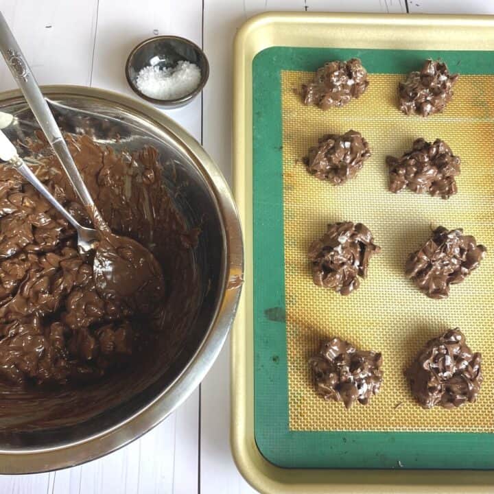 A bowl of chocolatey cashews with mounds piled on a sheet pan.