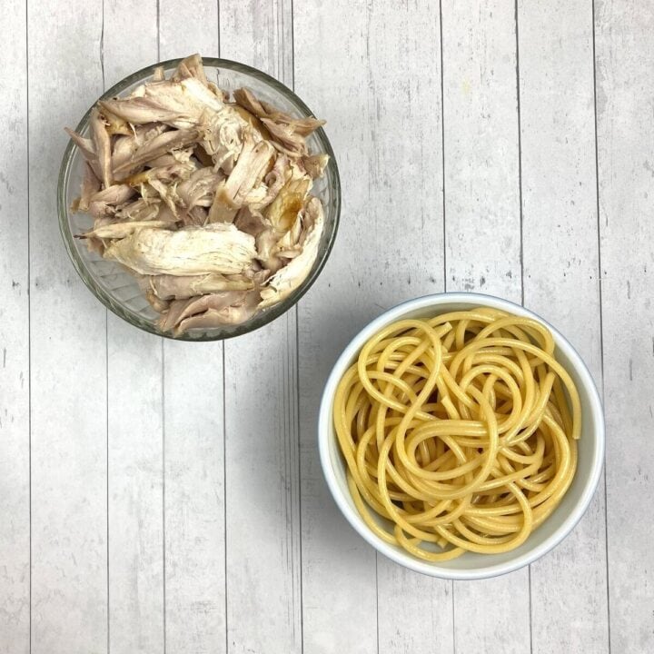 Two bowls on a table with pasta and rotisserie chicken,