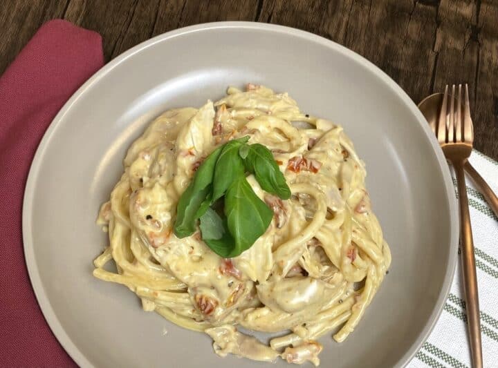 A bowl of marry me chicken pasta with a fork and spoon.