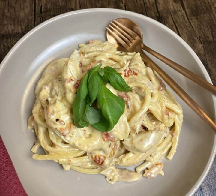 A fork and spoon sitting inside a bowl filled with marry me chicken pasta.