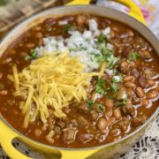 A yellow pot filled with hearty chili topped with cheese and onions.