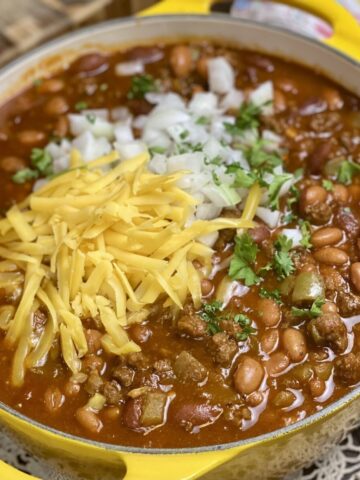 A yellow pot filled with hearty chili topped with cheese and onions.