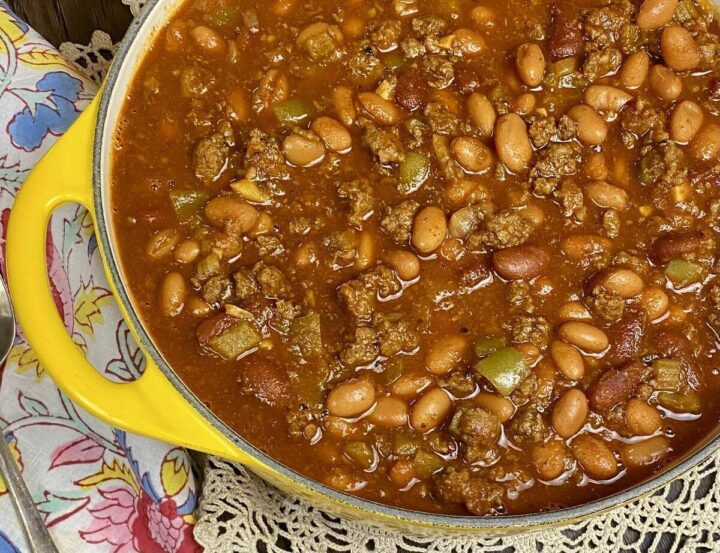 A yellow dutch oven filled with a batch of beef chili with a colorful napkin alongside.