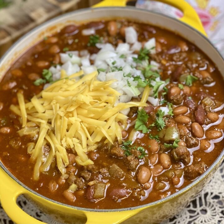 A yellow pot of chili with onions, cheese and parsley topping.