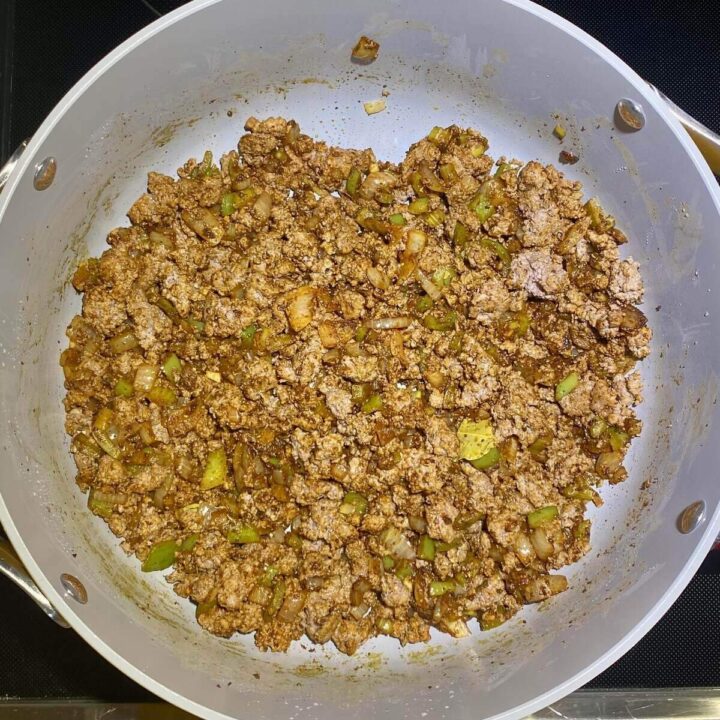 A pot cooking ground beef and vegetables with seasoning.