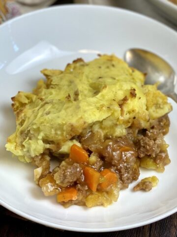 A serving of gluten free shepherd's pie in a ceramic bowl with a spoon.