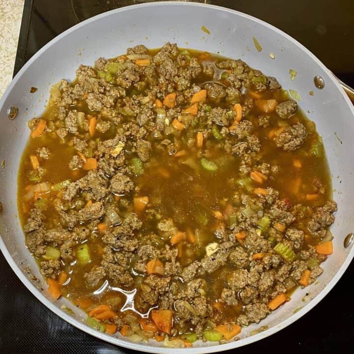 A skillet on the stove with cooked vegetables, meat, and beef broth. 