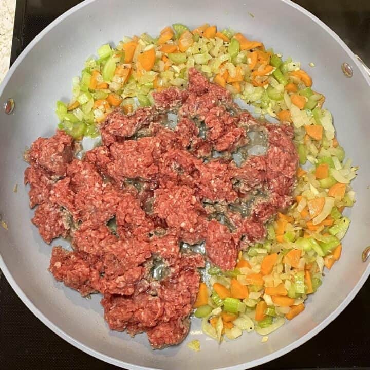 A skillet on the stove cooking vegetables and ground meat.