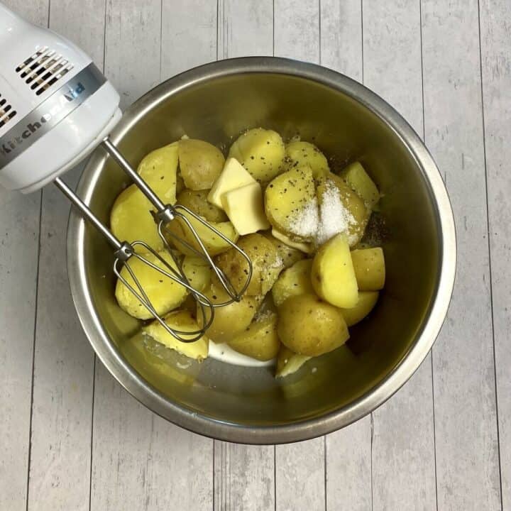 Boiled potatoes in a bowl with a hand mixer.