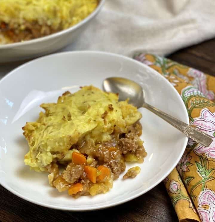 A serving of shepherds pie in a dish with a spoon and napkin.