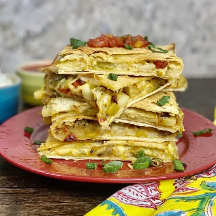 Five square potato quesadillas stacked up on a plate.