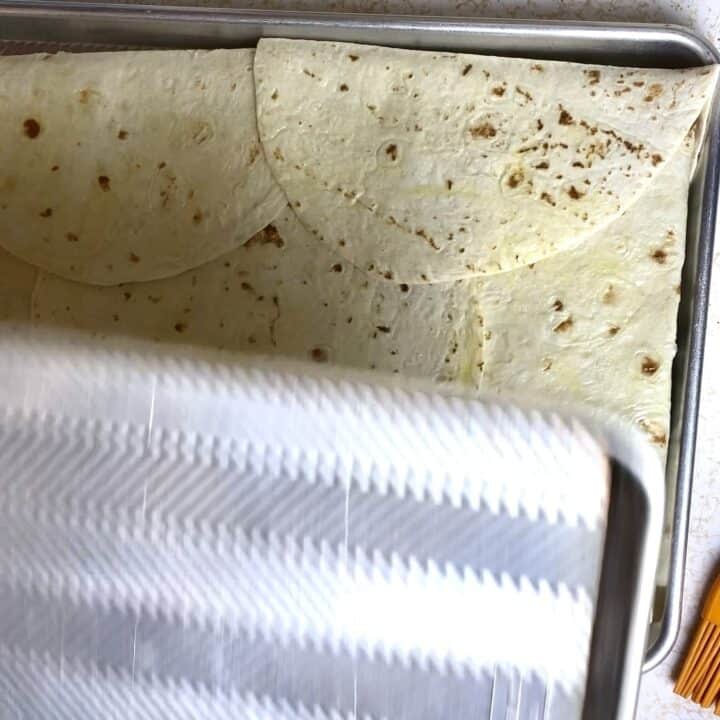 A second sheet pan being placed on top of the quesadillas de papa in the first sheet pan.