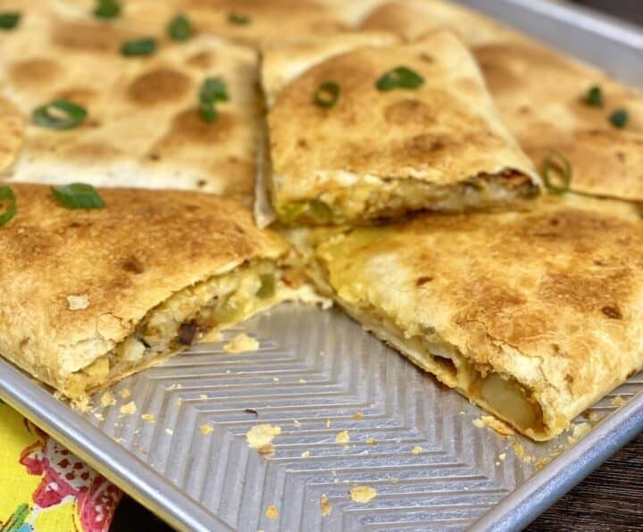 A close-up view of potato quesadilla in a sheet pan with piece cut out.