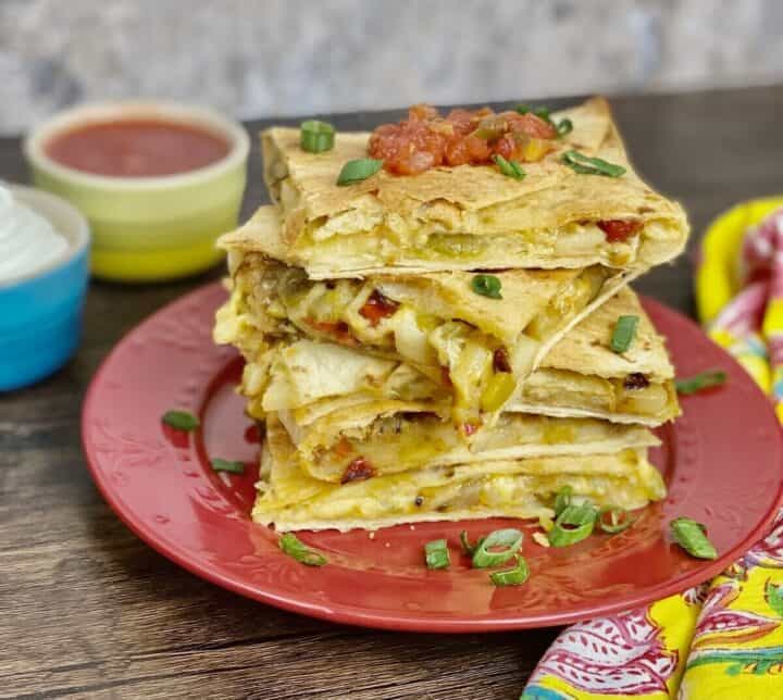 Five quesadillas stacked up on a plate with salsa and sour cream.