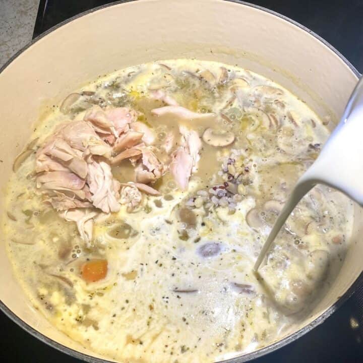 Cream pouring into a pot of chicken and wild rice soup.