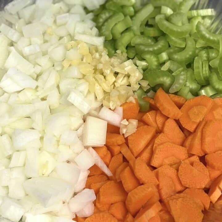 A closeup of diced onions, carrots, celery, and garlic.